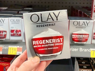 a hand holding a jar of face cream in a box in a store
