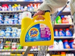 hand holding a bottle of tide simply detergent in front of walmart cart