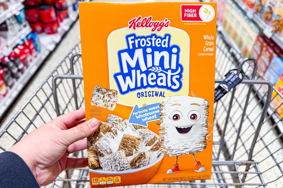 hand holding a box of frosted mini wheats cereal in a shopping cart