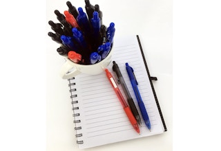 Different colored pens on a cup and on a notebook