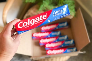 person holding colgate cavity protection toothpaste near box