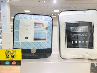 two different comforters sitting next to each other on a shelf by a clearance sign