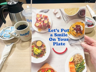Someone holding an IHOP menu that says "Let's put a smile on your plate"