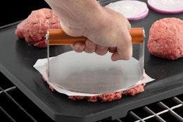 Cuisinart 6" Stainless Steel Smashed Burger Press being used by a person on the grill.