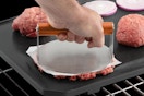 Cuisinart 6" Stainless Steel Smashed Burger Press being used by a person on the grill.