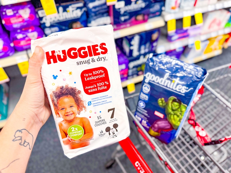 person holding a package of huggies snug & dry diapers over a cart with goodnites diapers in it