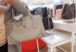 woman holds tan coach bag on arm in store