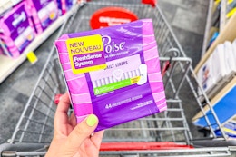 person holding a pack of poise pads over a cart