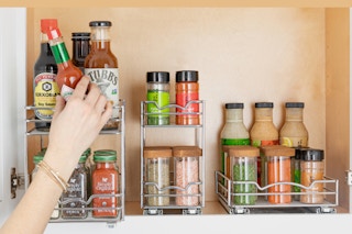 A cabinet has three different sized pull-out organizers inside, full of spices and sauces