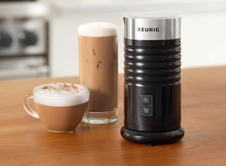 a milk frother on a table next to a cup of coffee