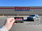 Someone holding up their Costco membership card in front of a Costco Business Center