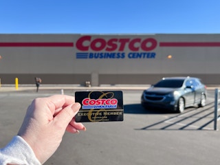 Someone holding up their Costco membership card in front of a Costco Business Center