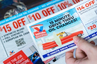 someone holding an oil change coupon above a pile of more coupons