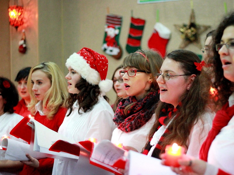 People standing in a line singing Christmas carols and wearing festive hats