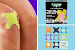 A knee with a bright yellow Curad bandage, a box of Curad, individual bandages out of the box