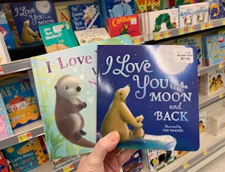 A hand holding two board books in a store aisle.