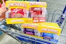 person holding a 6-pack of pizza lunchables over a cart with cracker stacker lunchables in it