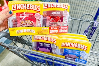 person holding a 6-pack of pizza lunchables over a cart with cracker stacker lunchables in it