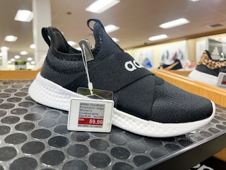 A black Adidas shoe with price tag sitting on a store shelf.