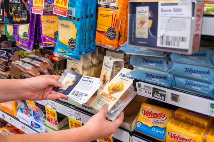 Hand holding coupons in front of cheese display