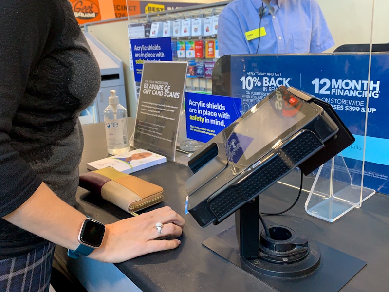 A person standing at a Best Buy checkout counter while an employee rings them up.