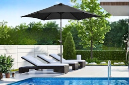 Lifestyle image of a black Ainfox patio umbrella outdoors near a pool