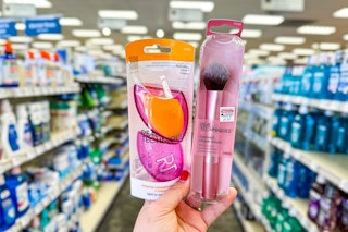 person holding a makeup sponge set and a makeup brush in an aisle