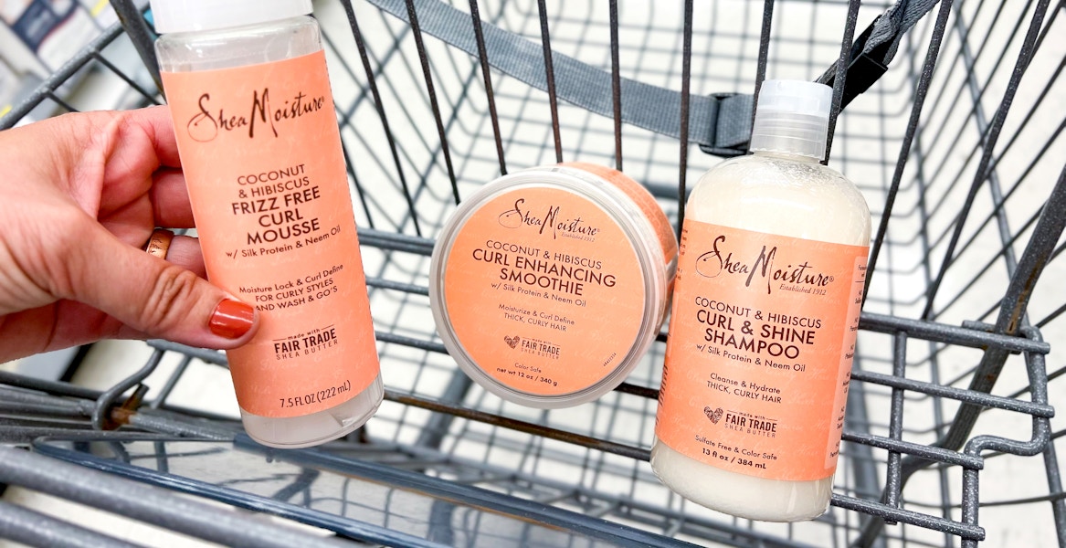 hand holding one bottle of SheaMoisture mousse next to curl smoothie and shampoo inside cart