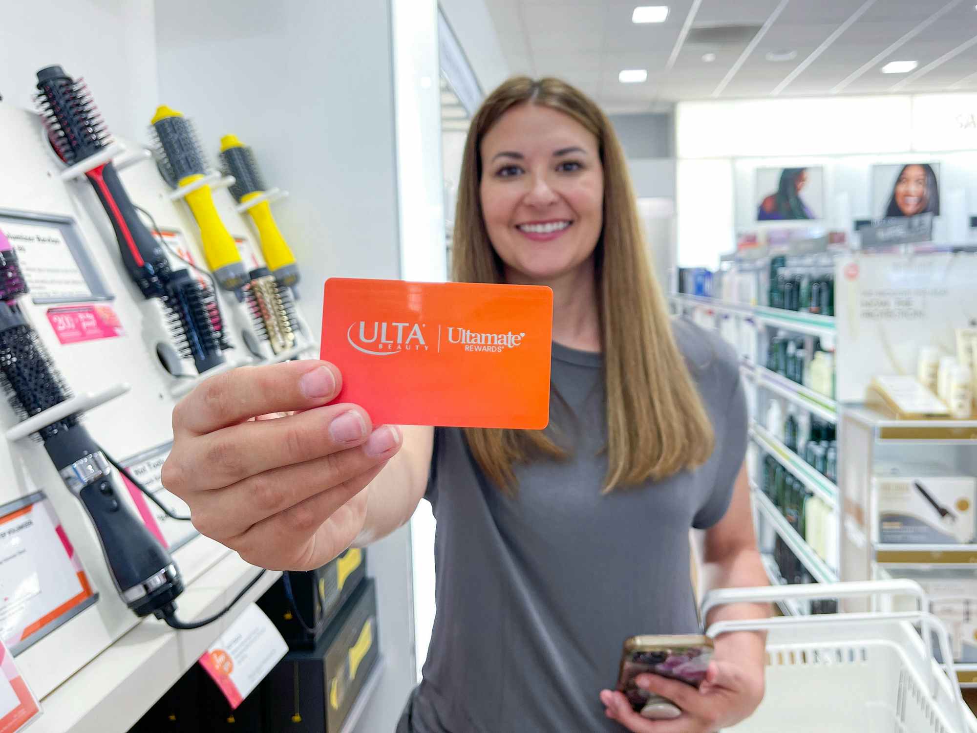 A person holding up their Ulta credit card in front of some styling tools on display