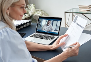 A woman looking at a resume with a person on a video call online.