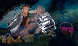 two people in front of a tent with an emergency thermal blanket around them
