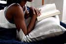 someone reading a book propped up on a satin pillowcase