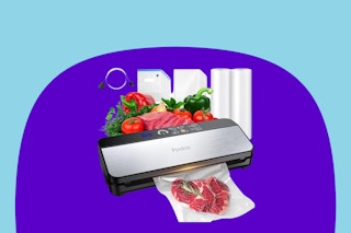A silver and black vacuum sealer machine with fresh vegetables and bag rolls behind it and a sealed bag of raw meat in front.