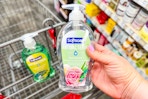 person holding softsoap hand soap over a cart with another soap in it