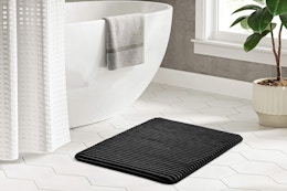 Lifestyle image of the black Mainstays foam bath rug in a bathroom setting