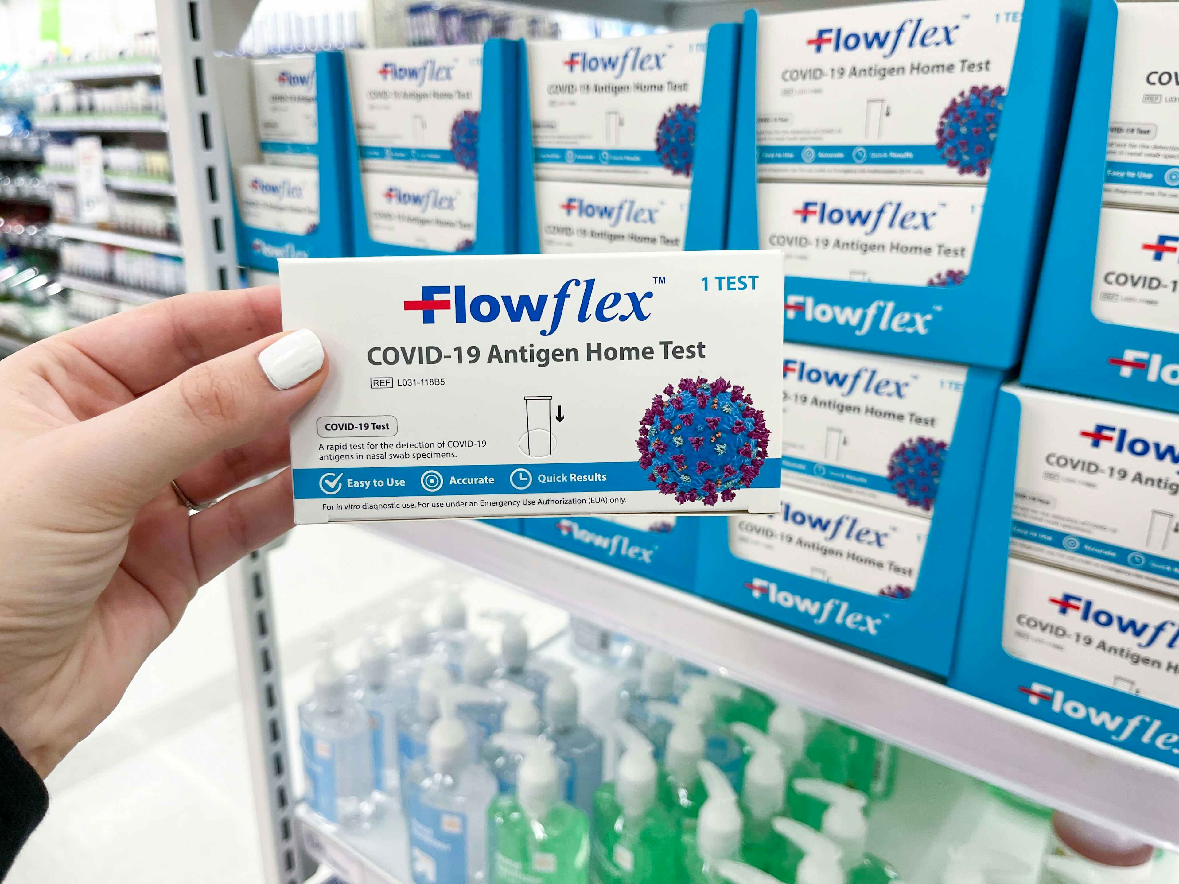 A person's hand holding up a box of FlowFlex Covid-19 Tests in front of in store display.