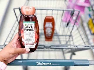 hand holding Garnier Whole Blends shampoo in front of cart with conditioner inside