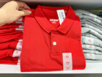 A person's hand holding up a children's school uniform polo shirt on a shelf at Old Navy.