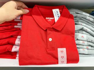 A person's hand holding up a children's school uniform polo shirt on a shelf at Old Navy.