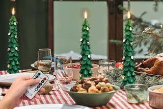 Person controlling the ZLCYFJIXV Flameless Christmas Tree Candles with Remote on a dinner table.