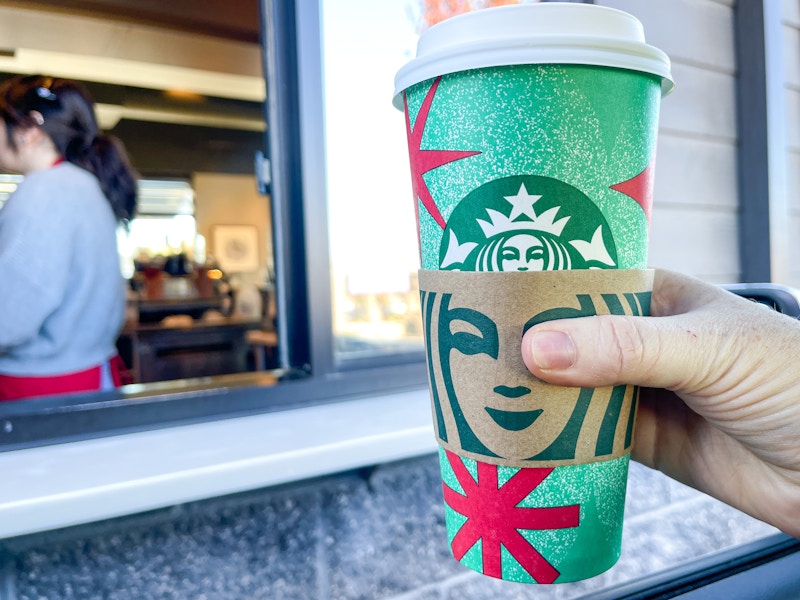 a person's hand holding up a starbucks holiday drink outside drive thru