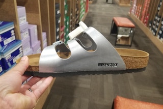 A person's hand holding a Birkenstock sandal in the aisle of a shoe store.