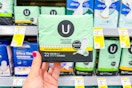 person holding a package of u by kotex pads in front of the shelf
