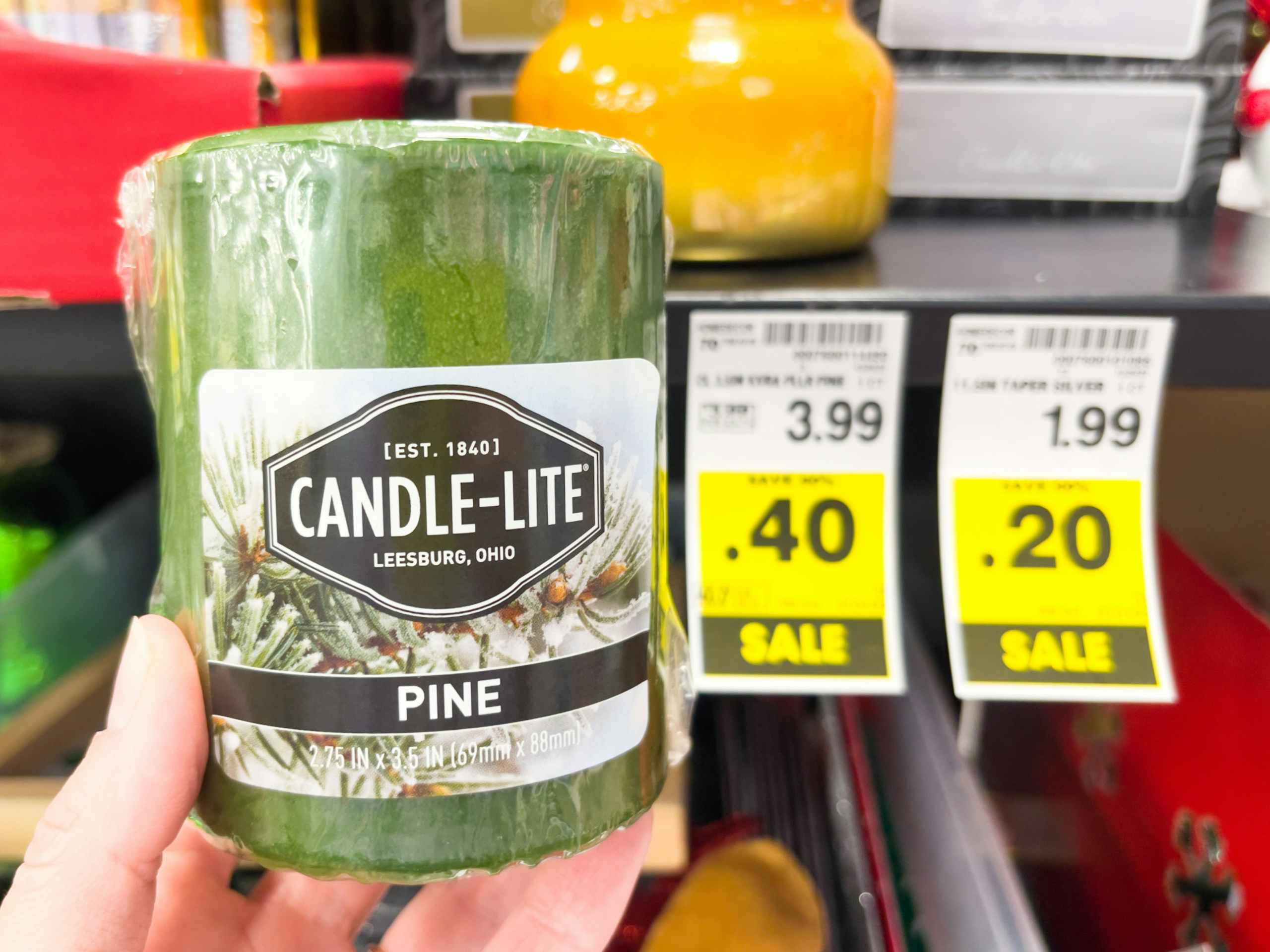 A candle held out by hand in front of price stickers.