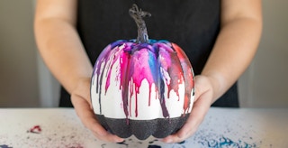 someone holding a pumpkin that has been decorated with melted crayons