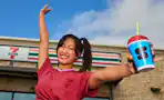 a woman standing outside of a 7-eleven holding a slurpee