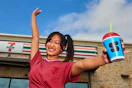 a woman standing outside of a 7-eleven holding a slurpee