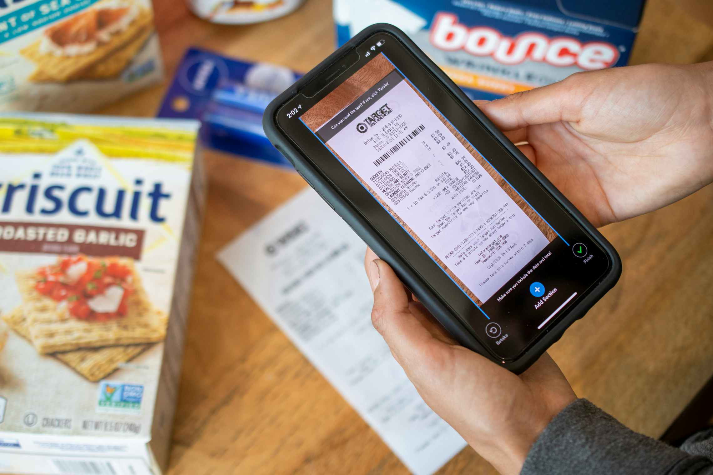 A person taking a photo of a Target receipt through the Checkout51 mobile app's scan feature. On the table next to the receipt are variou...