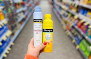 hand holding two bottles of neutrogena sunscreen spray