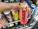 hand holding can of Truly in front of store refrigerator
